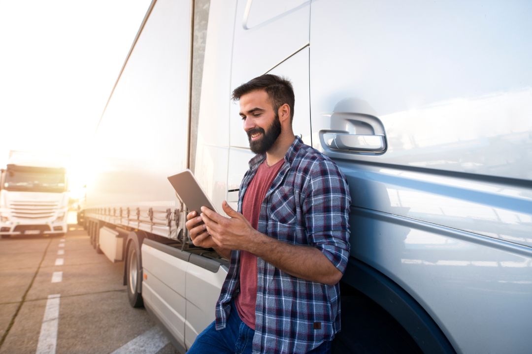 Professional truck driver checking his route on tablet computer and standing by long vehicle. Transportation service.