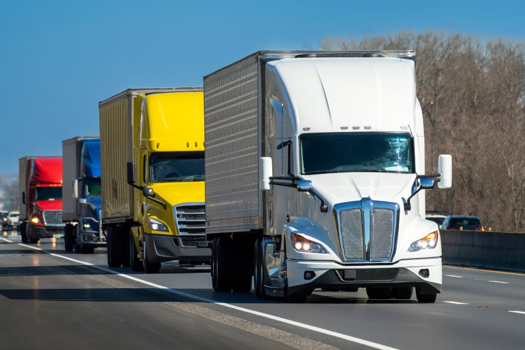 Horizontal shot of a color convoy of heavy semi trucks on the highway.