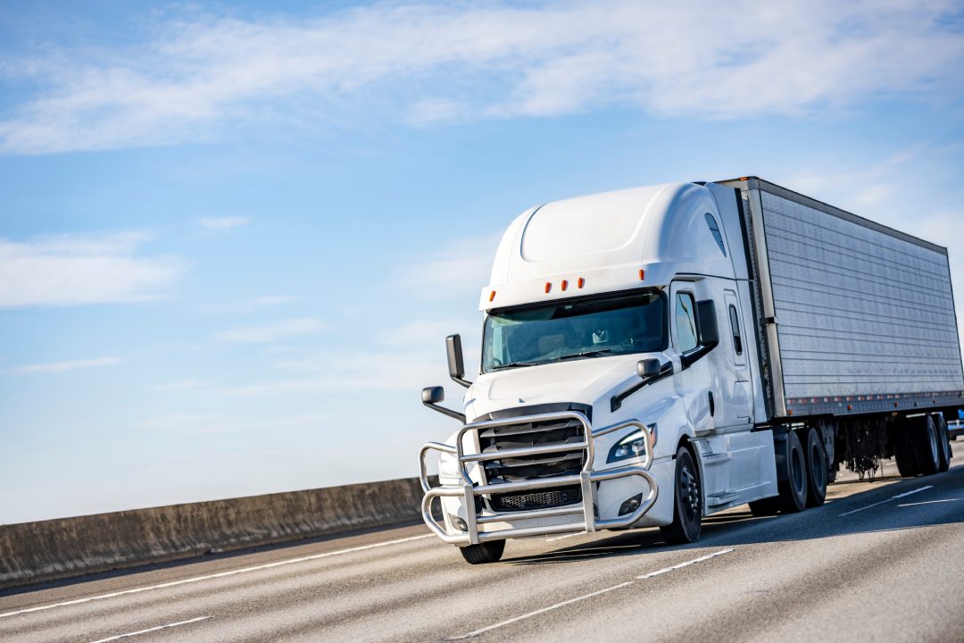 Comercial de gran camión blanco industrial de larga distancia semirremolque de transporte de carga congelada en el refrigerador semirremolque de conducción en la carretera carretera interestatal multilínea con una dirección de tráfico.