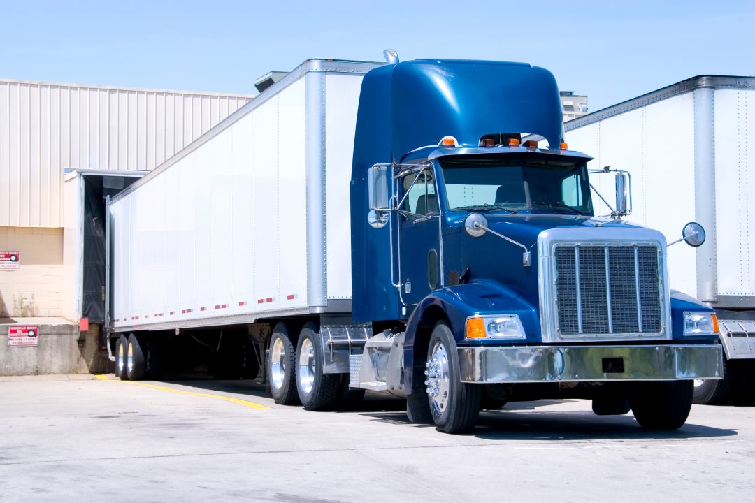 This is a picture of 18 wheeler semi truck loading at a warehouse building.