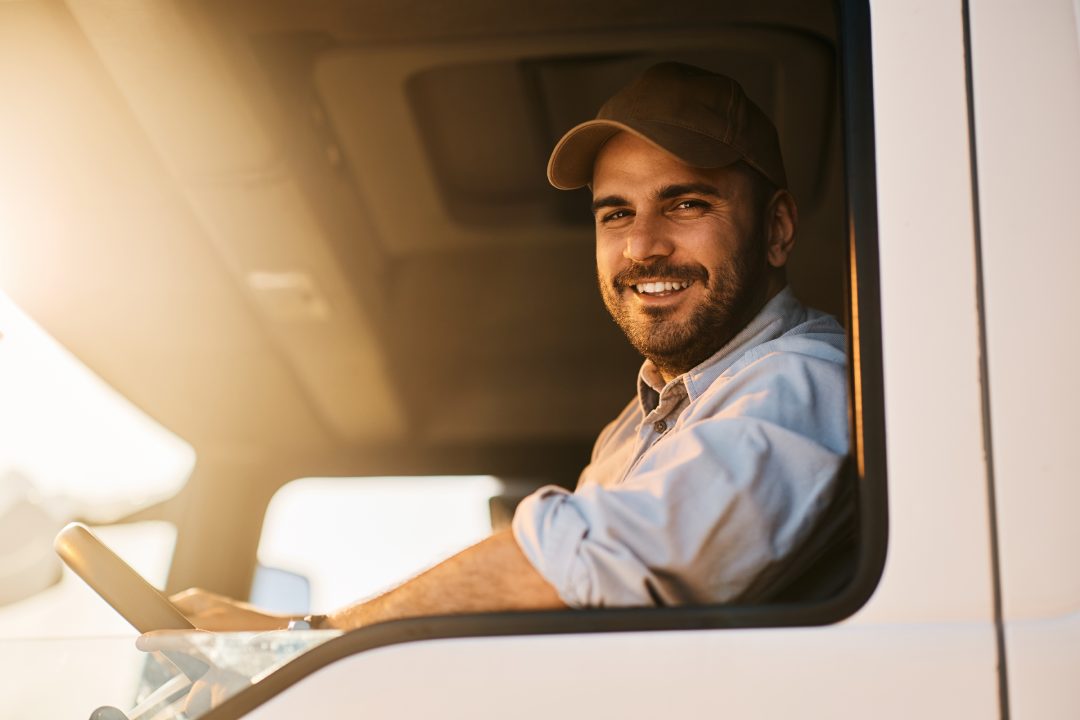 Happy truck driver sitting in vehicle cabin and looking at camera.