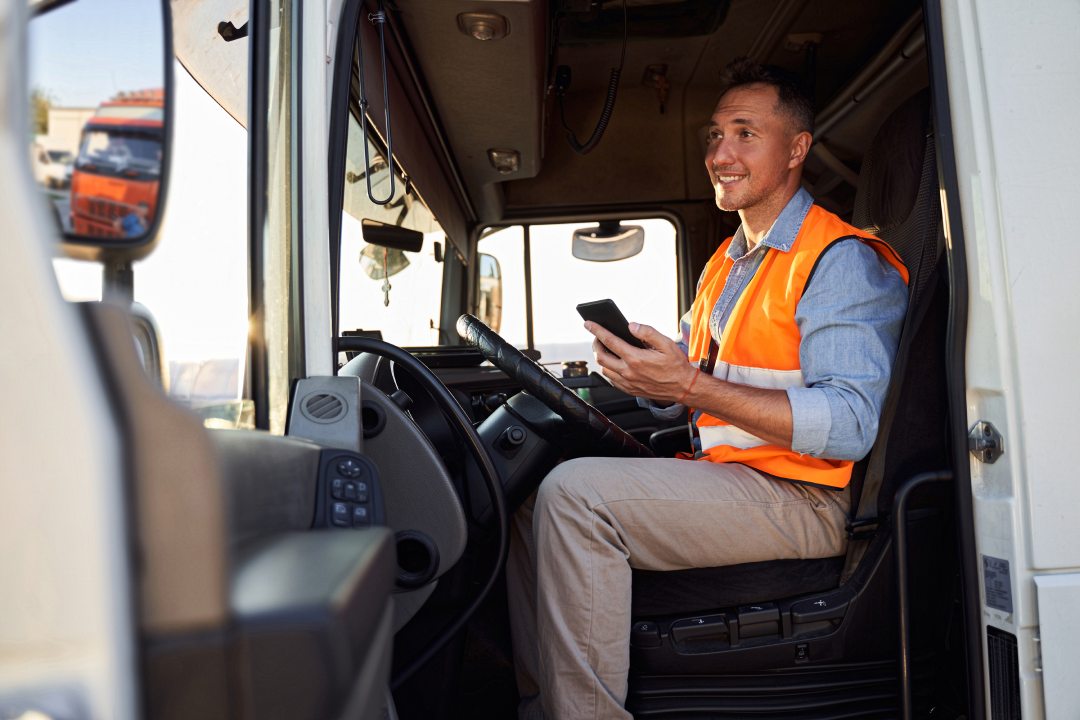 Forwarder or truck driver in drivers cap holding mobile phone