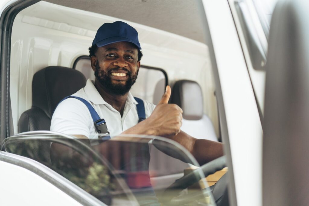 Hombre en el camión con el pulgar hacia arriba y sonriendo a la cámara mientras está sentado en el asiento del conductor.