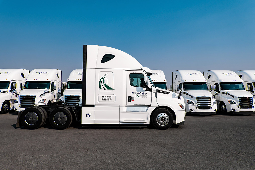 Mexcaltruck: A lineup of semi trucks parked in a lot, highlighting cold chain logistics for summer border crossings.