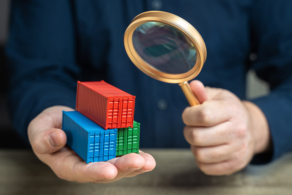 A person uses a magnifying glass to inspect containers, emphasizing the need for compliance training in logistics teams.