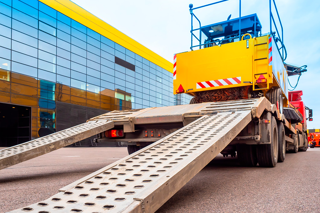 A large truck with a flatbed trailer and crane, used for relocating equipment from Tijuana to US manufacturing hubs.